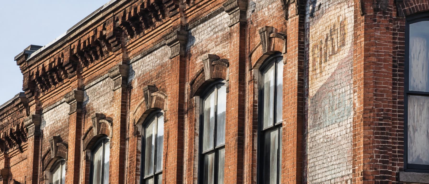 Corbelled brick cornice, arched window hoods, and a faded painted wall sign