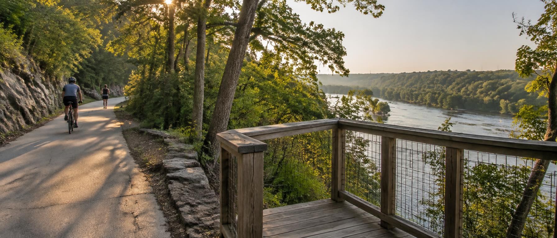 Cyclist and runner on a paved greenway beside a wooden river overlook