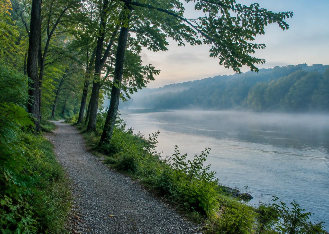 Wooded trail beside a calm river at Riverwalk-style recreation