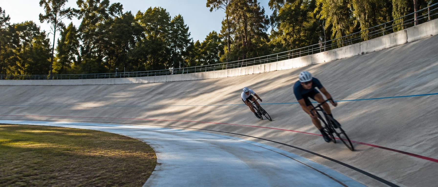 Track cyclists leaning into the banked curve of an outdoor concrete velodrome
